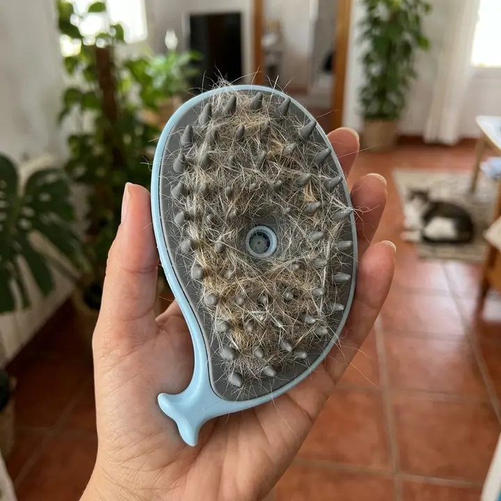 Cepillo de vapor azul con las púas llenas del pelo suelto recogido, en la palma de una mano (imagen ilustrativa)